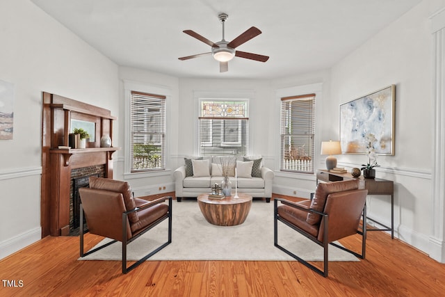 living room with a fireplace, light wood-type flooring, and ceiling fan