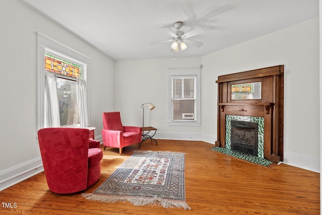 living area with hardwood / wood-style floors, a tiled fireplace, and ceiling fan