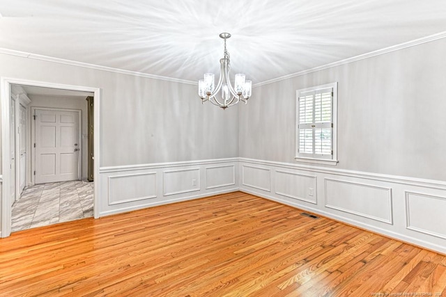 spare room featuring an inviting chandelier, light hardwood / wood-style flooring, and crown molding