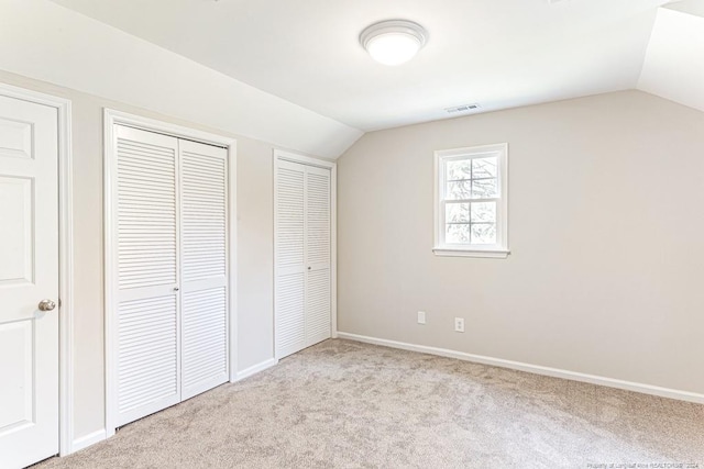 unfurnished bedroom featuring light carpet, two closets, and lofted ceiling