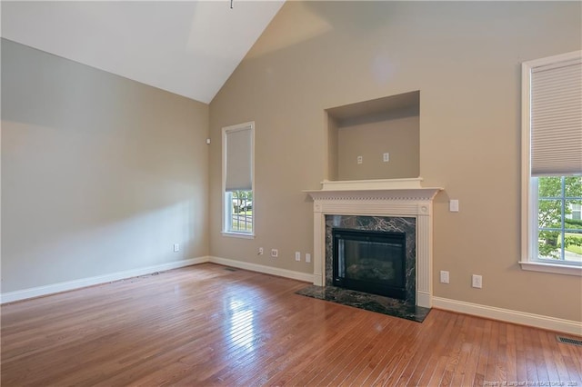 unfurnished living room featuring a wealth of natural light, high vaulted ceiling, a premium fireplace, and light wood-type flooring