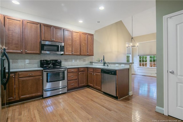 kitchen with appliances with stainless steel finishes, tasteful backsplash, sink, hanging light fixtures, and kitchen peninsula