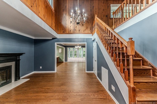 staircase featuring wood-type flooring, a notable chandelier, crown molding, and a high ceiling