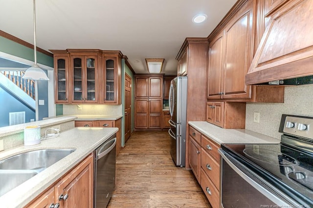 kitchen featuring ornamental molding, light hardwood / wood-style floors, custom exhaust hood, appliances with stainless steel finishes, and decorative light fixtures