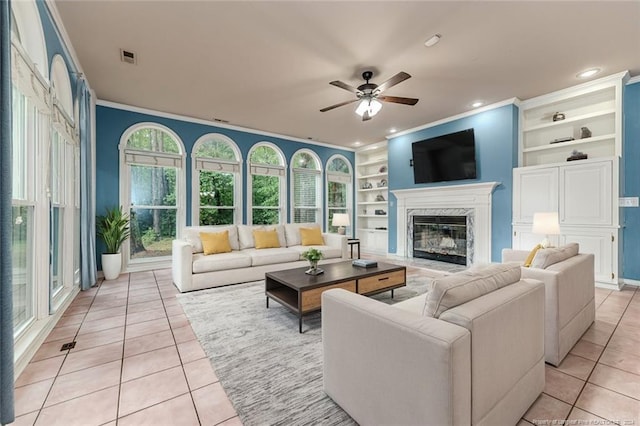 tiled living room featuring ceiling fan, crown molding, built in features, and a high end fireplace