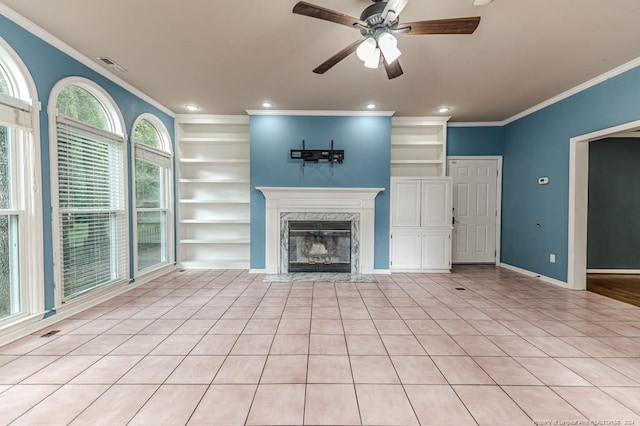 unfurnished living room with built in features, ceiling fan, a fireplace, ornamental molding, and light tile patterned floors