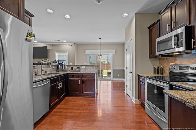 kitchen featuring dark wood-type flooring, sink, light stone countertops, hanging light fixtures, and appliances with stainless steel finishes