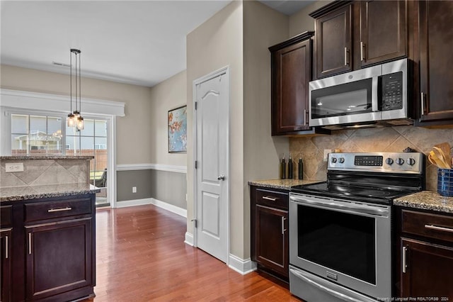 kitchen with tasteful backsplash, wood-type flooring, decorative light fixtures, appliances with stainless steel finishes, and light stone countertops