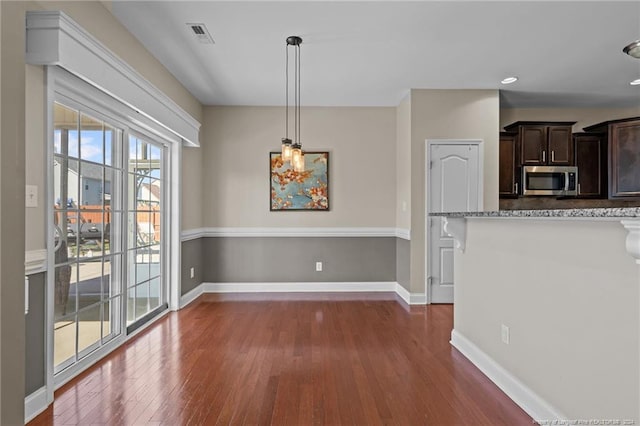 kitchen with dark brown cabinetry, decorative light fixtures, dark hardwood / wood-style floors, and light stone counters