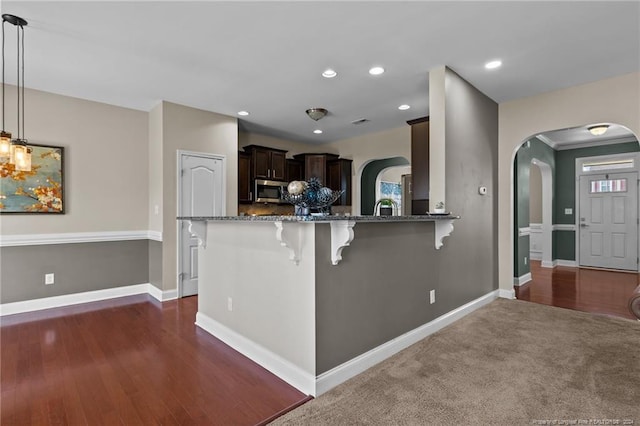 kitchen with dark hardwood / wood-style flooring, kitchen peninsula, pendant lighting, dark brown cabinets, and a kitchen bar