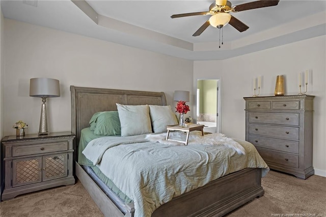 bedroom featuring a raised ceiling, light colored carpet, and ceiling fan