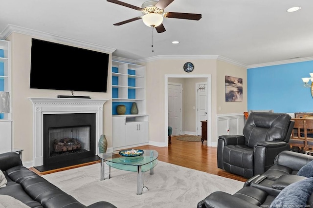 living room featuring wood-type flooring, ceiling fan, built in shelves, and crown molding