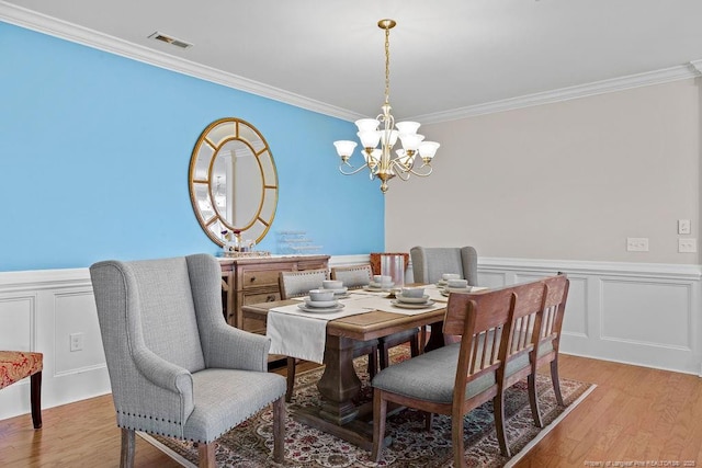 dining room with an inviting chandelier, ornamental molding, and light wood-type flooring