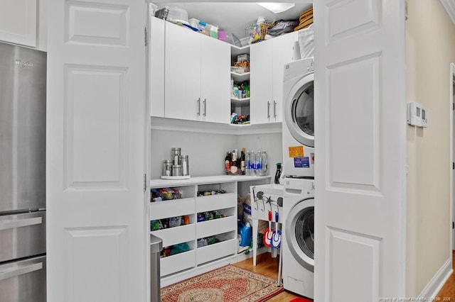 laundry room featuring cabinets, light hardwood / wood-style flooring, and stacked washer / dryer