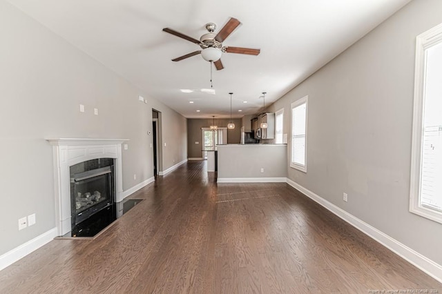 unfurnished living room featuring ceiling fan with notable chandelier and dark wood-type flooring