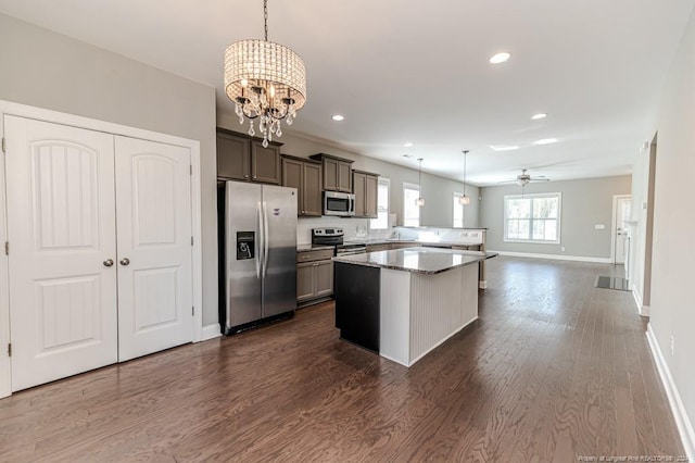 kitchen with dark hardwood / wood-style flooring, stainless steel appliances, light stone countertops, hanging light fixtures, and a center island