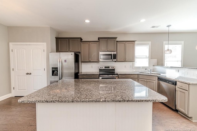 kitchen with light stone countertops, light wood-type flooring, stainless steel appliances, and hanging light fixtures