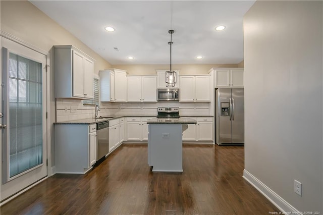 kitchen with a kitchen island, dark wood-type flooring, pendant lighting, appliances with stainless steel finishes, and backsplash