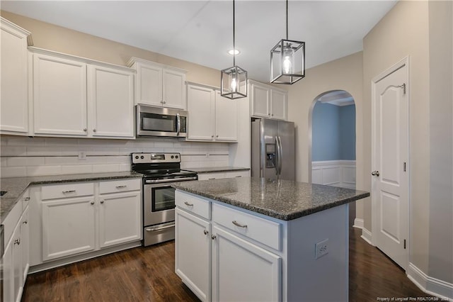 kitchen featuring dark stone counters, stainless steel appliances, dark hardwood / wood-style floors, white cabinets, and a center island