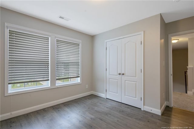 unfurnished bedroom with hardwood / wood-style flooring, multiple windows, and a closet