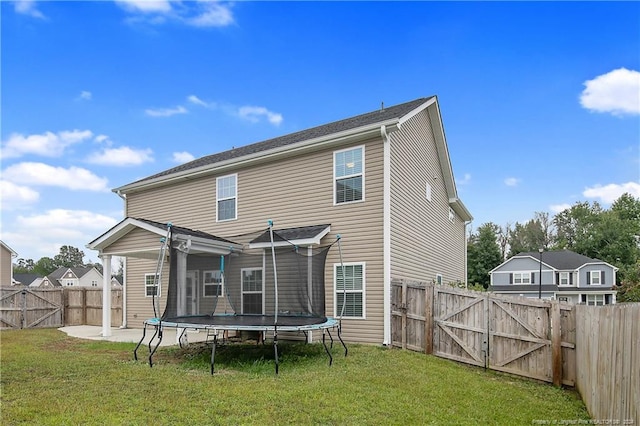 rear view of property with a trampoline, a lawn, and a patio area