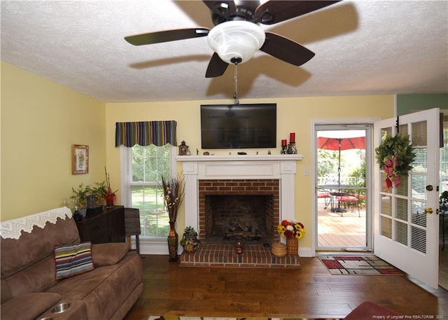 living room with dark wood-type flooring, a brick fireplace, a textured ceiling, and a healthy amount of sunlight