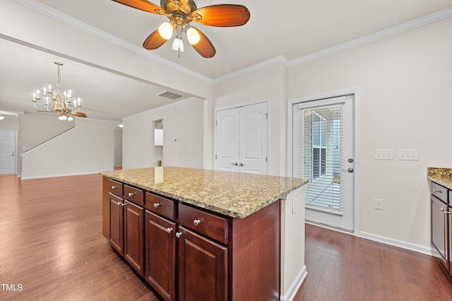 kitchen featuring a center island, decorative light fixtures, light stone counters, crown molding, and dark hardwood / wood-style floors