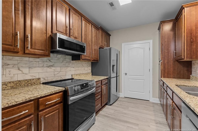 kitchen featuring light wood-type flooring, tasteful backsplash, light stone counters, sink, and appliances with stainless steel finishes