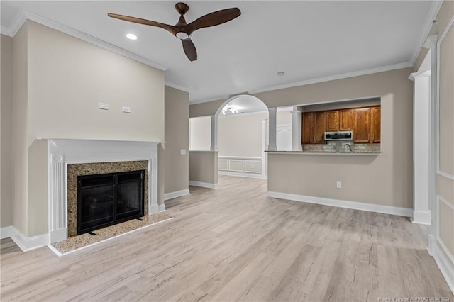 unfurnished living room featuring a high end fireplace, crown molding, light hardwood / wood-style flooring, and ceiling fan