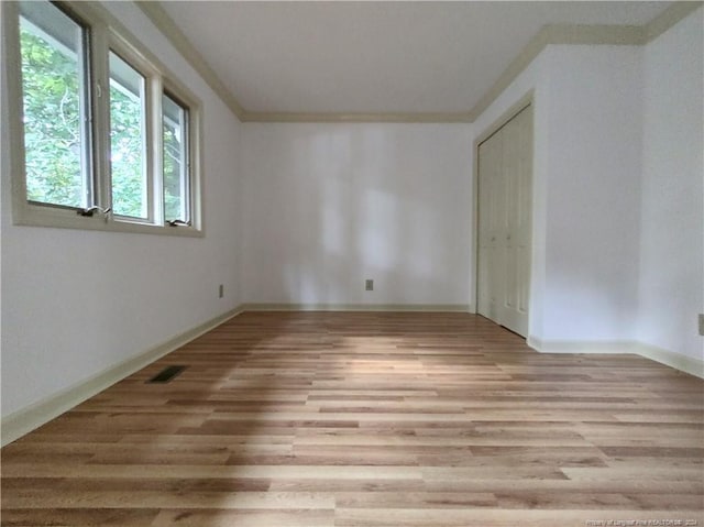 empty room featuring light wood-type flooring and crown molding