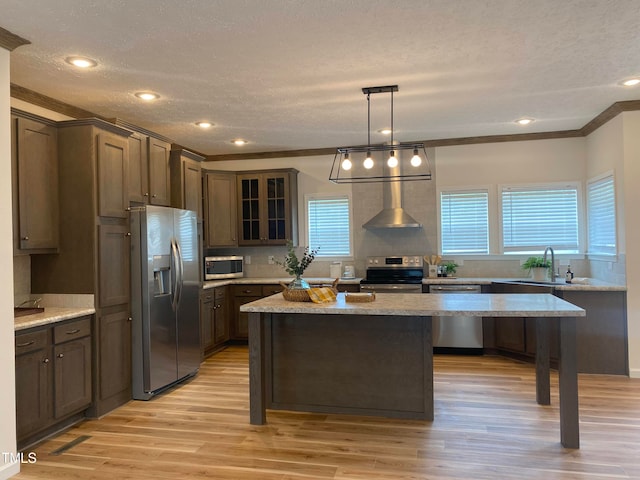 kitchen with stainless steel appliances, wall chimney range hood, light stone counters, and light wood-type flooring