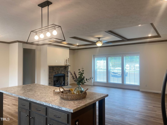 kitchen with a raised ceiling, a kitchen island, decorative light fixtures, dark hardwood / wood-style floors, and a fireplace