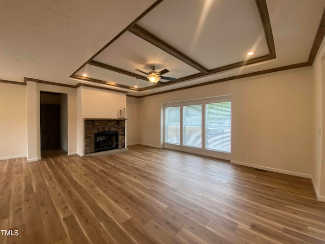 unfurnished living room featuring a stone fireplace, wood-type flooring, and a raised ceiling