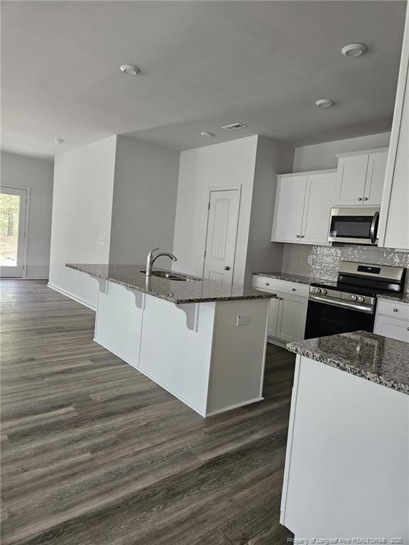 kitchen with dark stone counters, dark wood finished floors, stainless steel appliances, and a sink