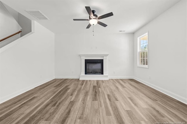 unfurnished living room featuring visible vents, a fireplace with raised hearth, baseboards, and wood finished floors