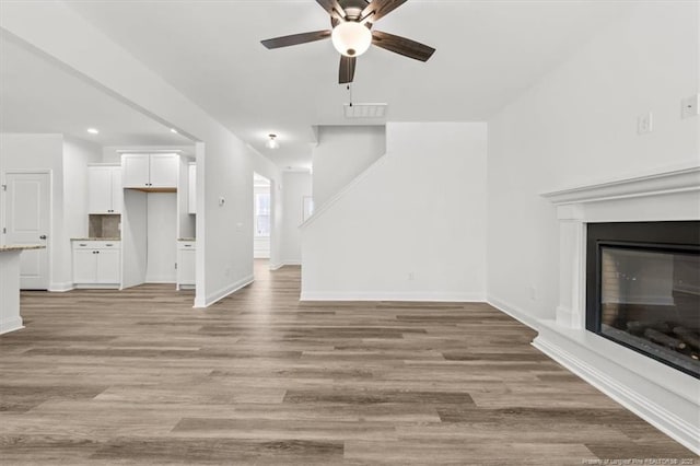 unfurnished living room featuring a glass covered fireplace, baseboards, ceiling fan, and light wood finished floors