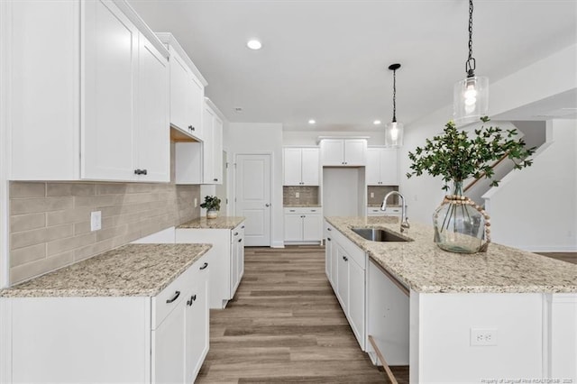 kitchen featuring light stone countertops, light wood-type flooring, white cabinetry, a sink, and recessed lighting