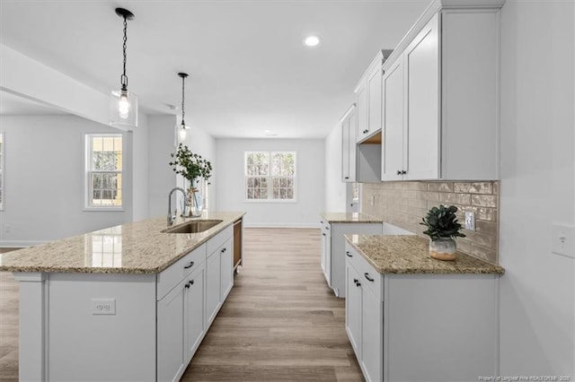 kitchen featuring light stone counters, backsplash, a sink, and light wood-style floors