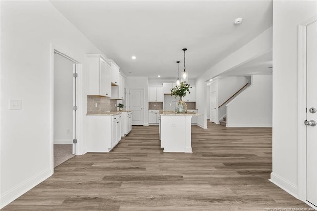 kitchen featuring baseboards, decorative backsplash, a kitchen island with sink, light wood-type flooring, and white cabinetry