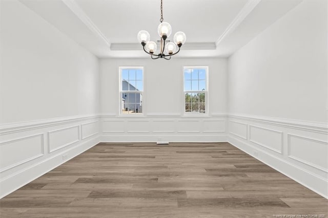 unfurnished dining area with ornamental molding, a tray ceiling, wood finished floors, and an inviting chandelier