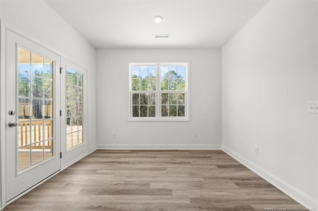 empty room with visible vents, a wealth of natural light, and wood finished floors