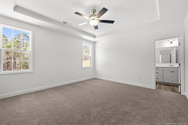 unfurnished bedroom with baseboards, a raised ceiling, ensuite bath, carpet flooring, and a sink