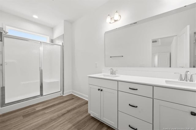 full bathroom featuring a stall shower, double vanity, a sink, and wood finished floors