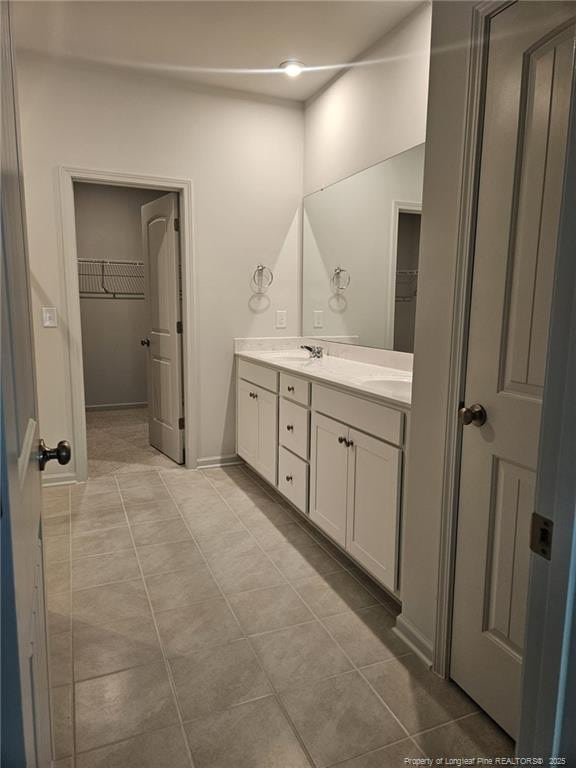 bathroom with double vanity, a spacious closet, tile patterned flooring, and a sink