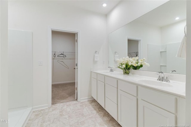 bathroom featuring recessed lighting, double vanity, a spacious closet, and a sink