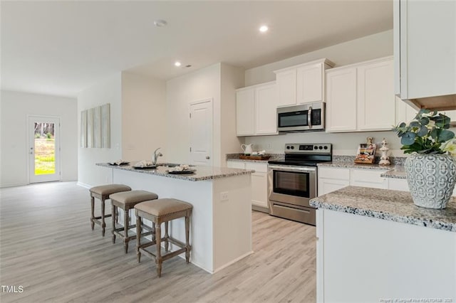 kitchen featuring an island with sink, appliances with stainless steel finishes, white cabinetry, and light stone counters