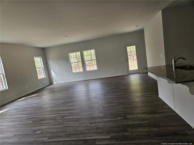 unfurnished living room featuring a sink, dark wood-style floors, and baseboards
