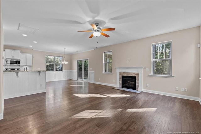 unfurnished living room featuring ceiling fan, ornamental molding, sink, dark wood-type flooring, and a fireplace