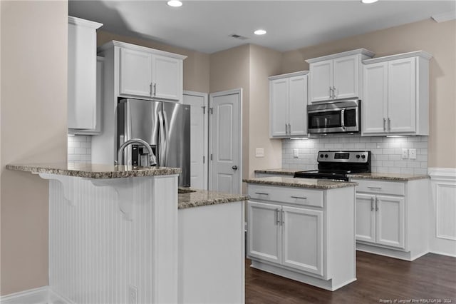 kitchen with appliances with stainless steel finishes, dark hardwood / wood-style flooring, stone countertops, and white cabinetry