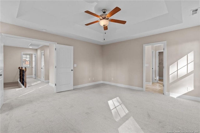 spare room featuring a raised ceiling, ceiling fan, and light carpet